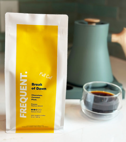 Bag of Break of Dawn full caf coffee from Frequent Coffee next to a cup of coffee