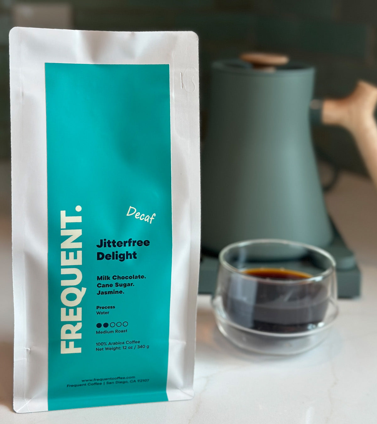 A bag of Jitterfree Delight Swiss Water Decaf coffee from Frequent next to a coffee cup