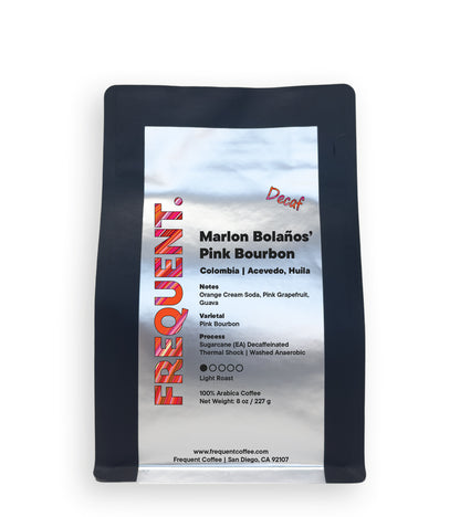 A bag of Marlon Bolaños' Pink Bourbon decaf coffee from Frequent Coffee on a plain white background. The packaging is black with a large metallic label showing the product details.