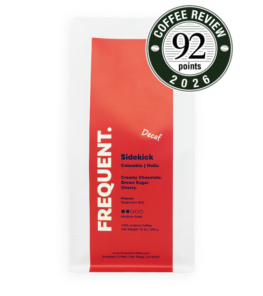 A bag of Frequent Coffee Decaf Sidekick coffee on a white background, featuring a red and white package with a green and white 'Coffee Review 92 points 2026' badge overlay in the top right corner.